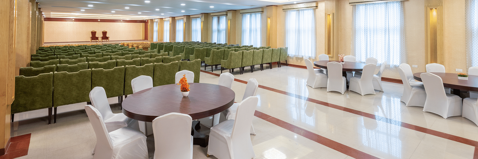A side angle shot of a banquet hall at DLS Tehri Club Resort featuring green sofas and round table.